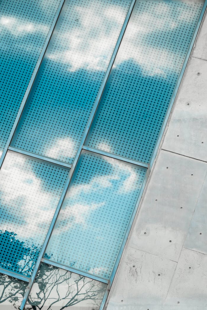 Cloud reflections on perforated glass windows with concrete wall contrast.